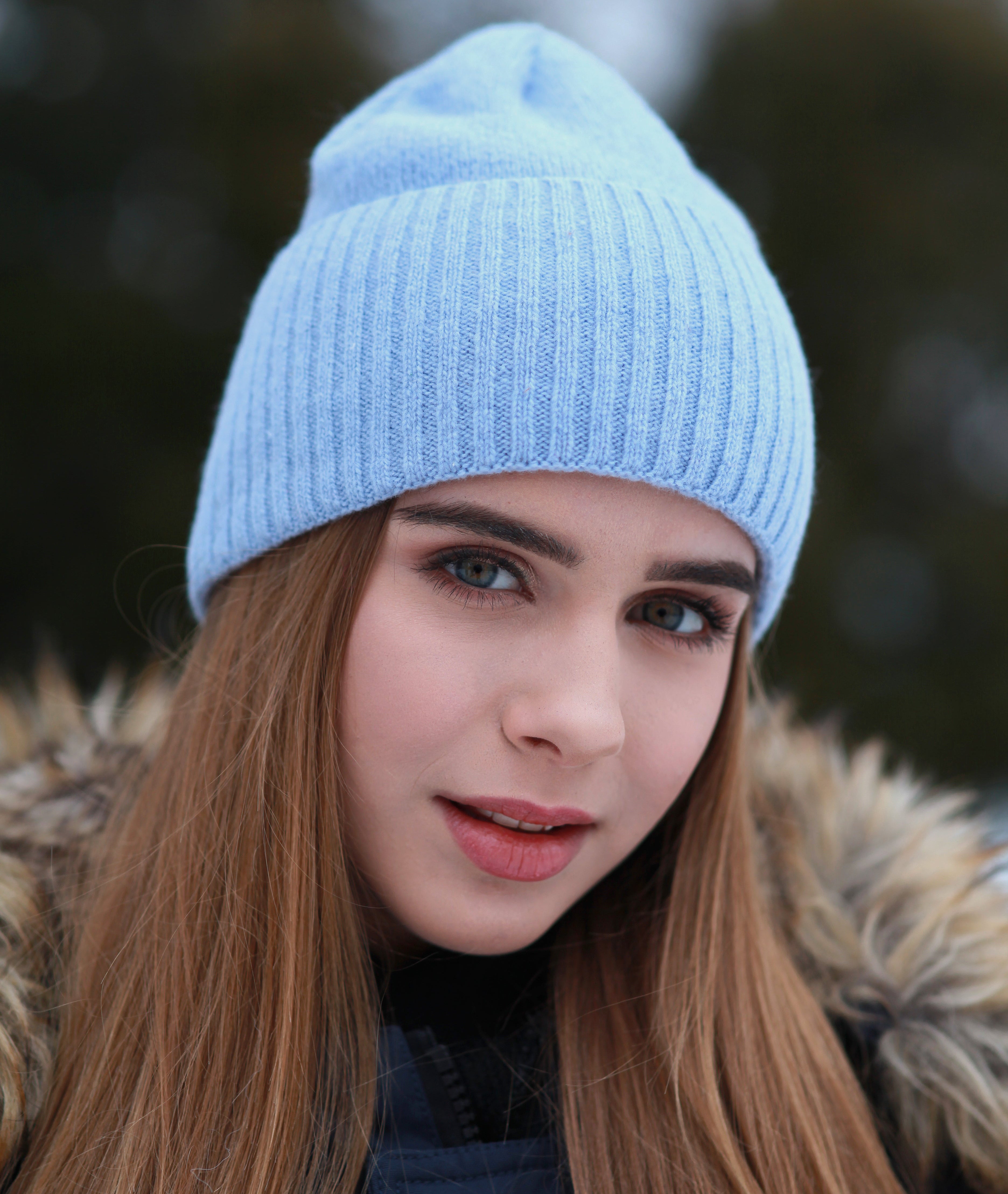 Woman wearing a blue knit beanie with a blurred natural background