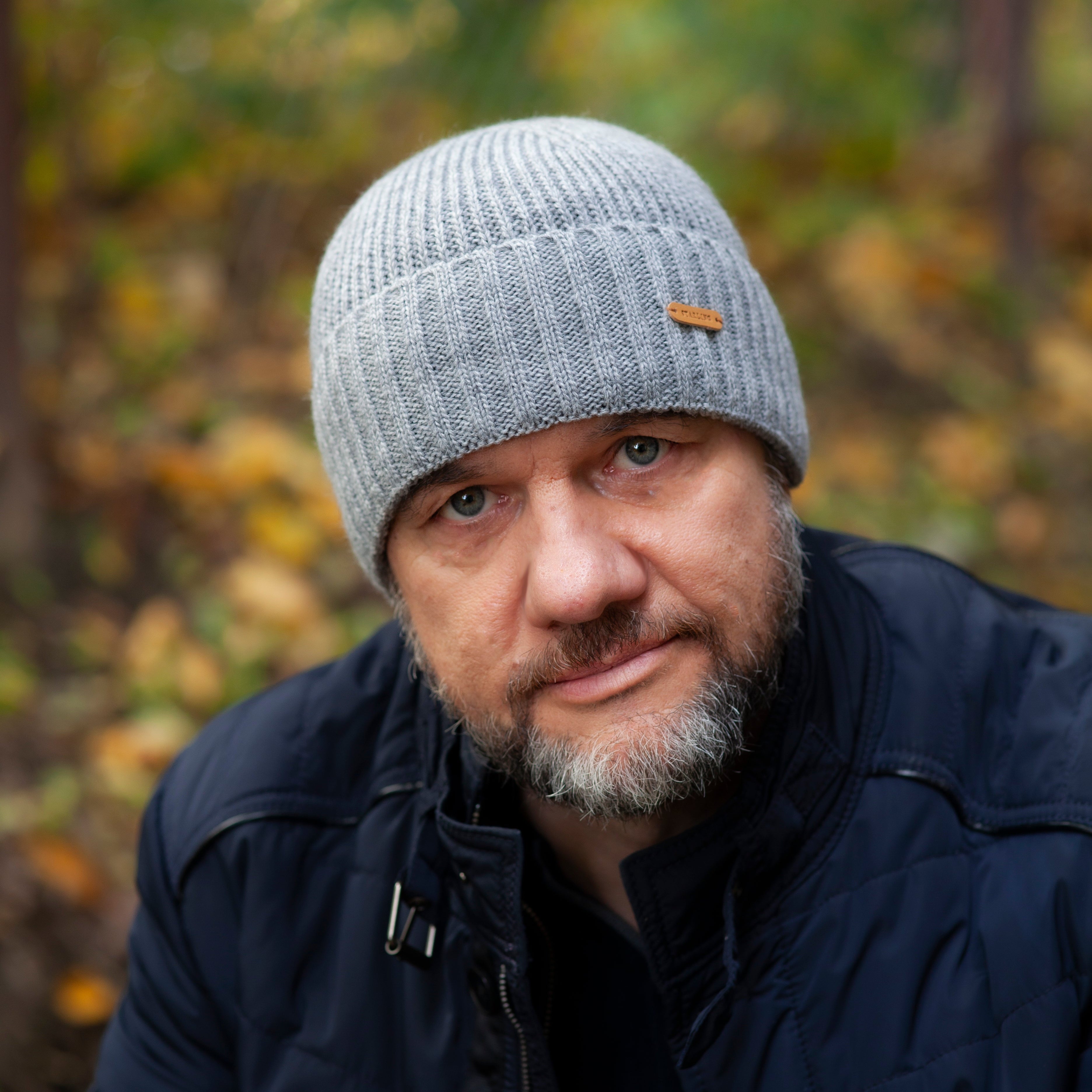 Man wearing a gray knit beanie and dark jacket in a forest setting