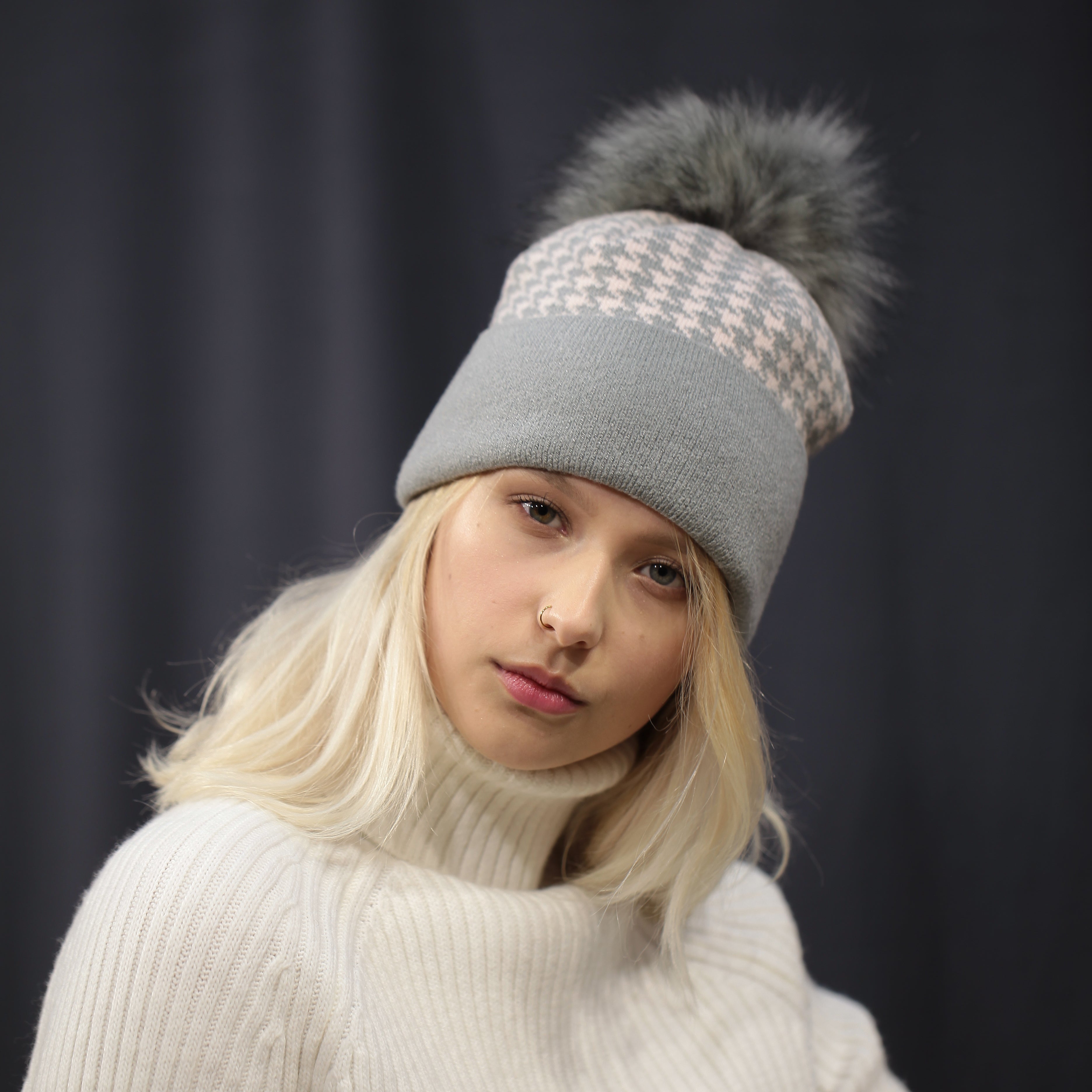 Person wearing a white sweater and gray beanie with pom-pom on a dark background