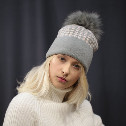 Person wearing a white sweater and gray beanie with pom-pom on a dark background