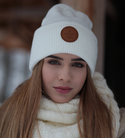 Close-up of a girl wearing a white beanie with a brown logo and a textured white scarf.