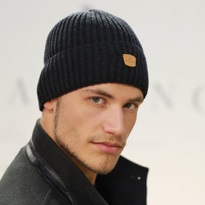 Person wearing a black beanie with a brand logo on a light background
