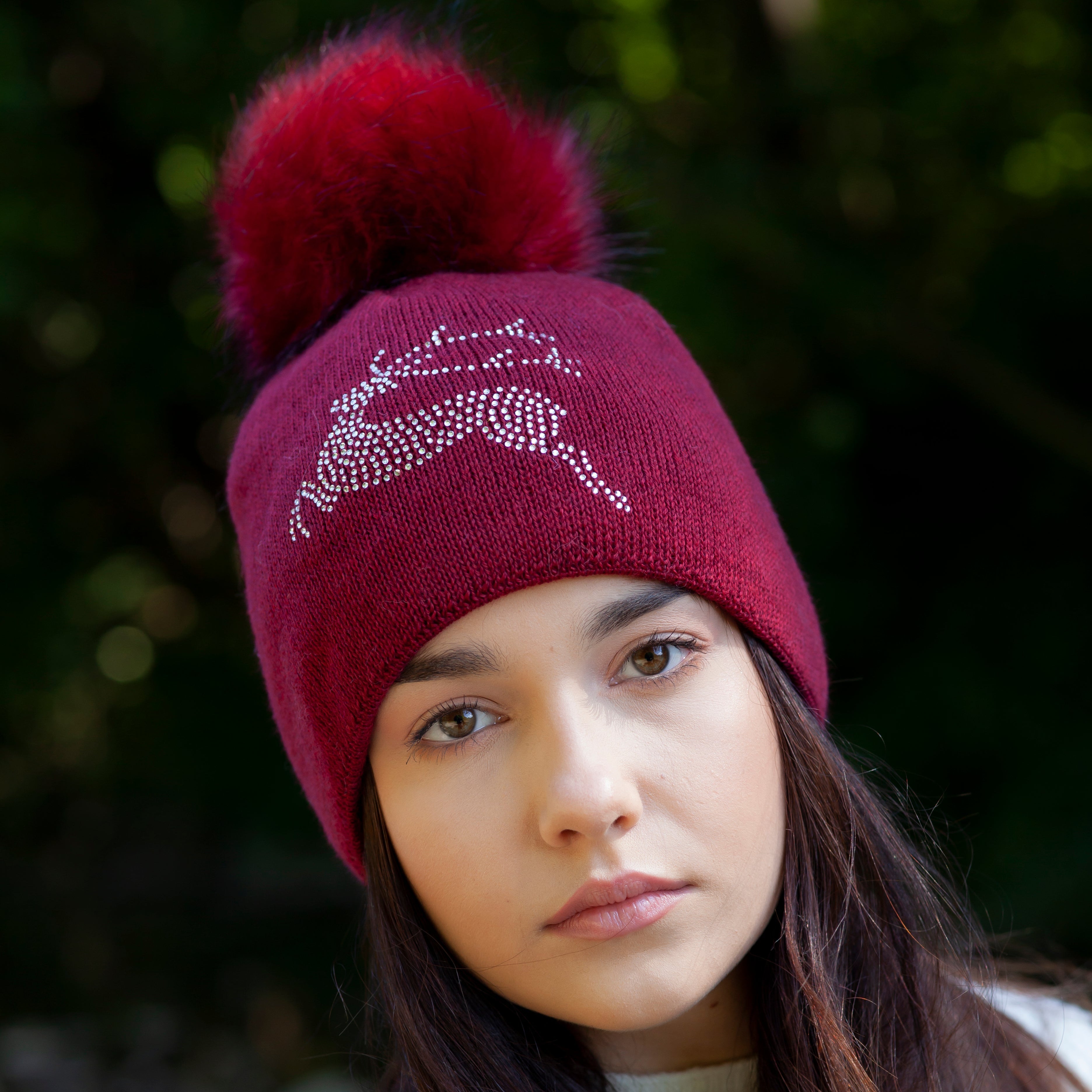 Woman wearing a maroon knit beanie with a red pom-pom and reindeer design, outdoors.