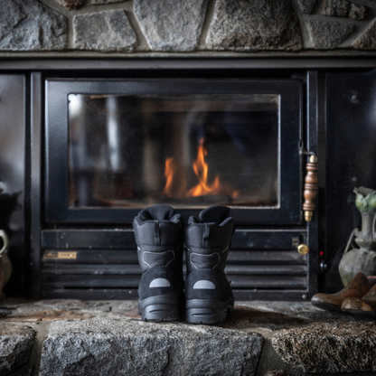Pair of black Attiba Eiger 2 men's snow boots warming by a fireplace, rear three-quarter lifestyle view