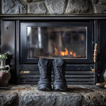 Pair of black Attiba Eiger 2 men's lace-up snow boots warming by a fireplace on a stone hearth, lifestyle view