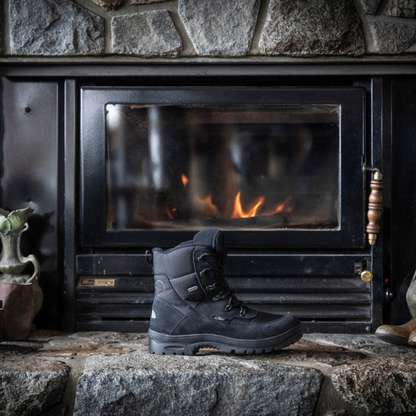 Black Attiba Eiger 2 men's lace-up snow boot on a stone hearth beside a lit fireplace, lifestyle view